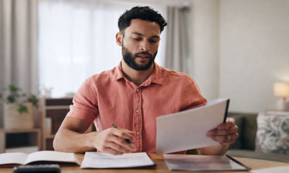 Muškarac sedi za stolom i pregledava dokumenta dok računa troškove i obaveze vezane za izdavanje stana