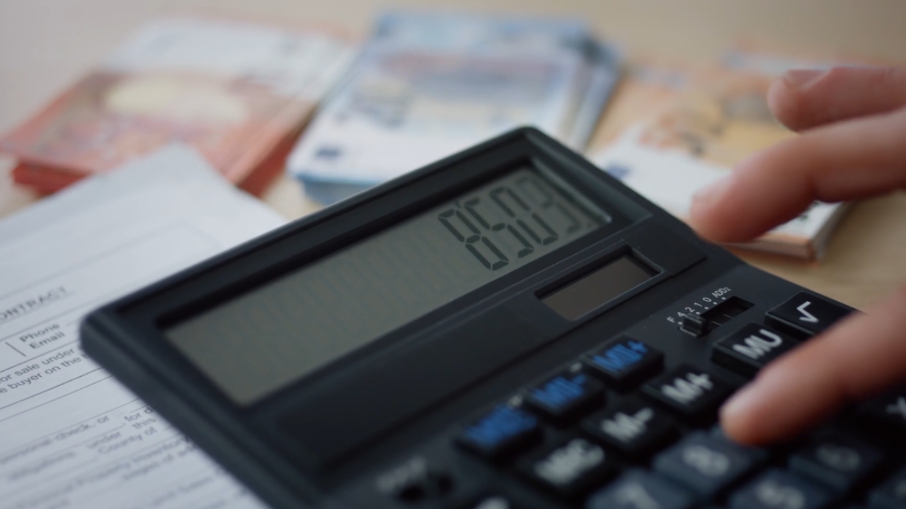 Osoba koristi kalkulator pored novčanica i finansijskih dokumenata