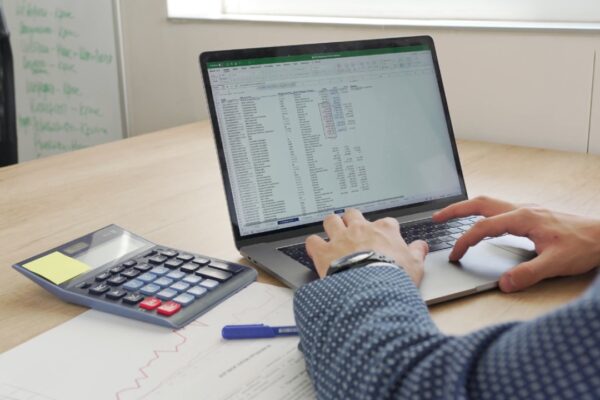 Osoba na laptopu analizira troškove uz kalkulator i poslovne izveštaje