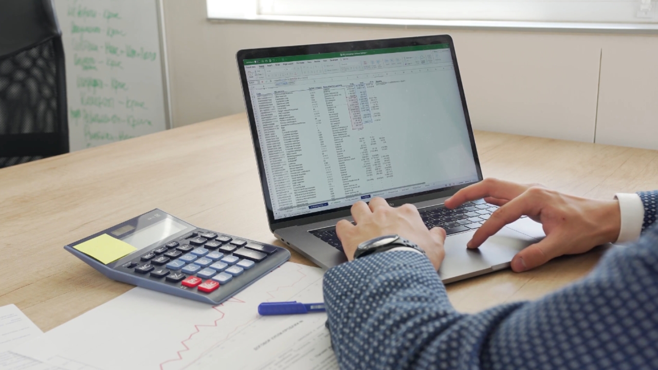 Preduzetnik proverava poslovne podatke na laptopu uz kalkulator i finansijsku dokumentaciju
