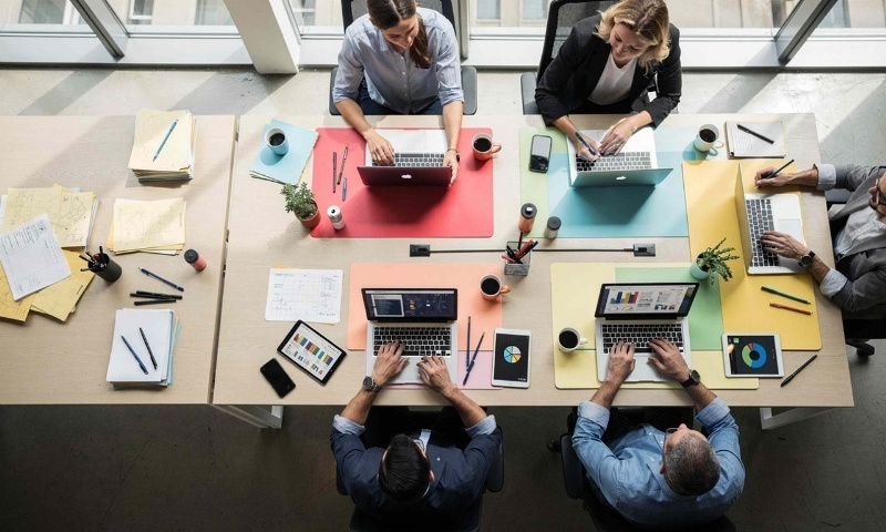 Petoro ljudi radi na laptopovima za zajedničkim stolom u modernom coworking prostoru.