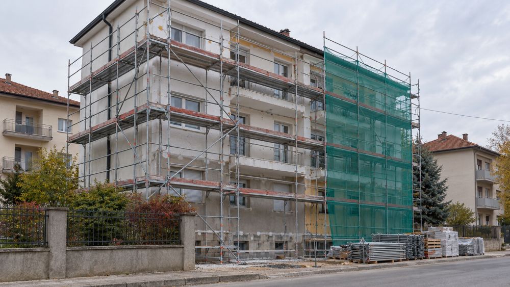 Metalna građevinska skela sa zaštitnom mrežom postavljena uz stambenu zgradu tokom obnove fasade.