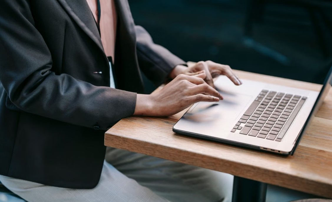 Osoba tamnom sakou koristi srebrni laptop za rad za drvenim stolom